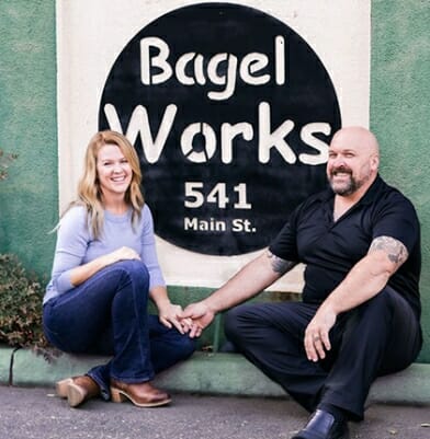 Bagel Works 541 Main St. Outside sign with the owners sitting in from of the sign holding hands