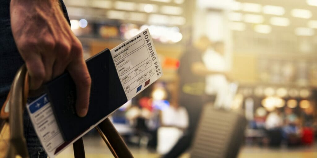 holding passport and boarding pass held by a man at an airport