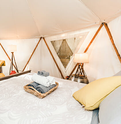 Reverie Retreat yurt interior - bed with rolled towels in a basket on top, pillows, 2 lamps