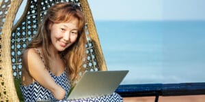 Lady with a stump right hand smiling at the camera in an egg hammock while working on her laptop