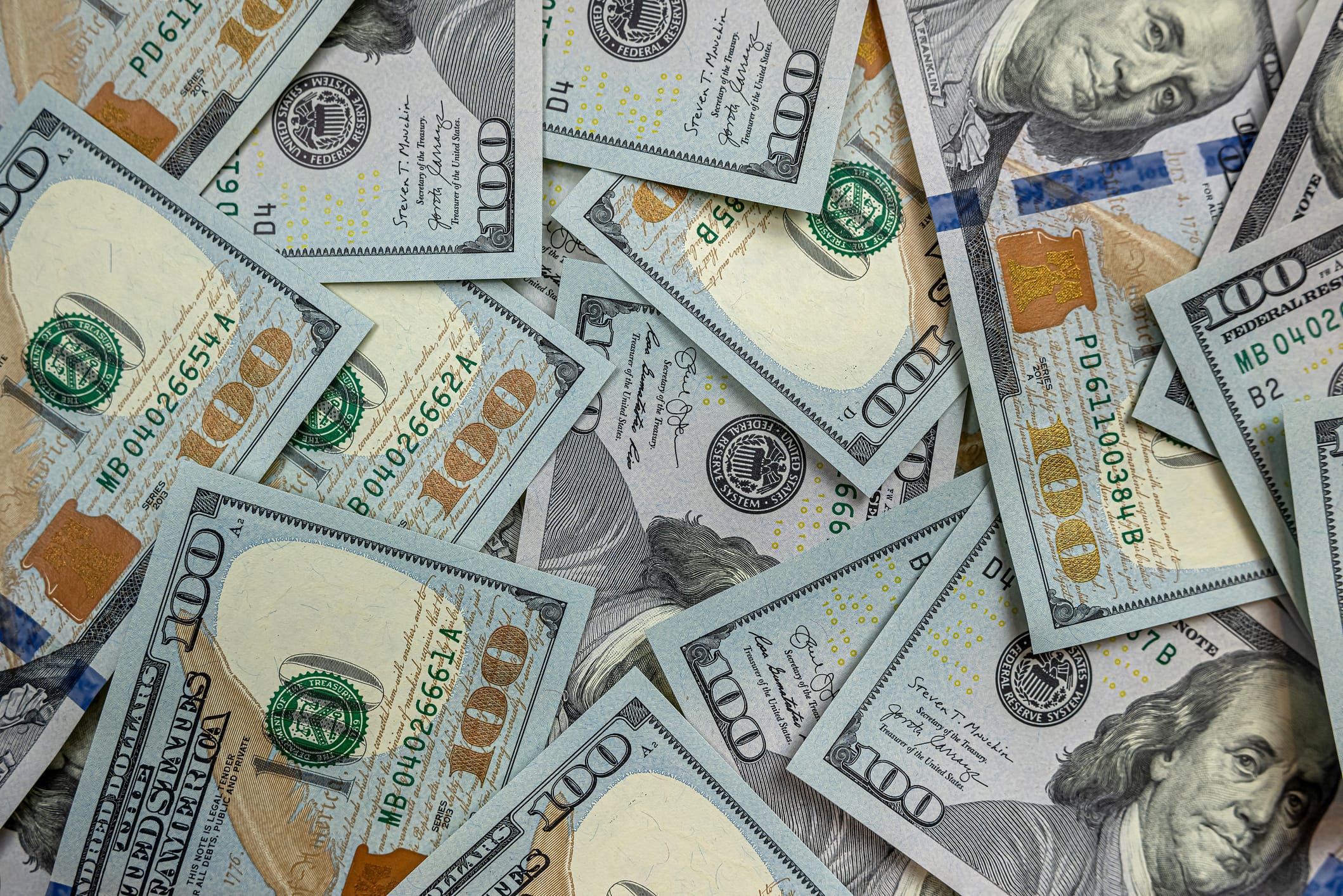 A scattered pile of U.S. one hundred dollar bills covering the background